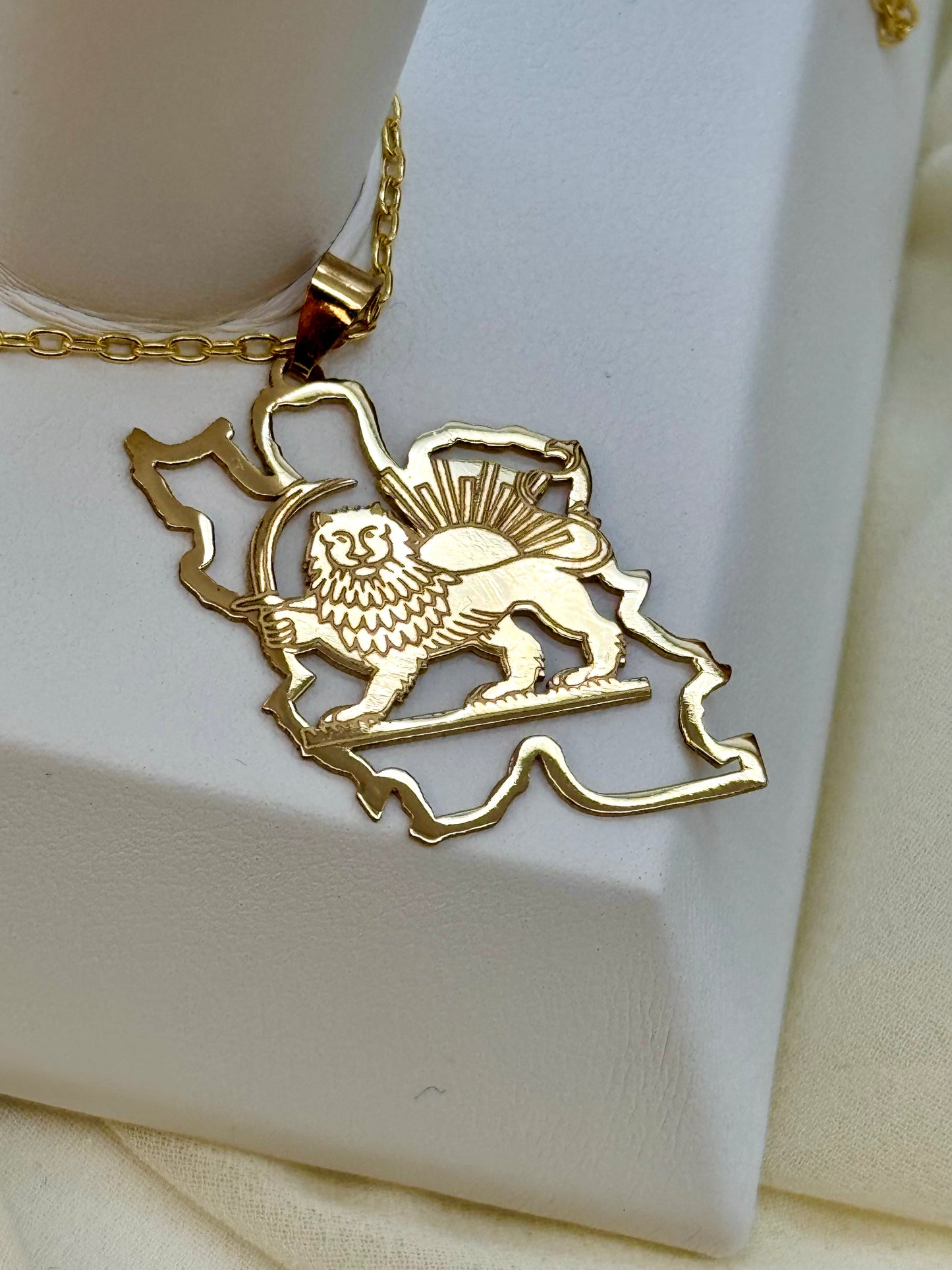 Gold Iran map necklace with a lion and sun on a white stand.