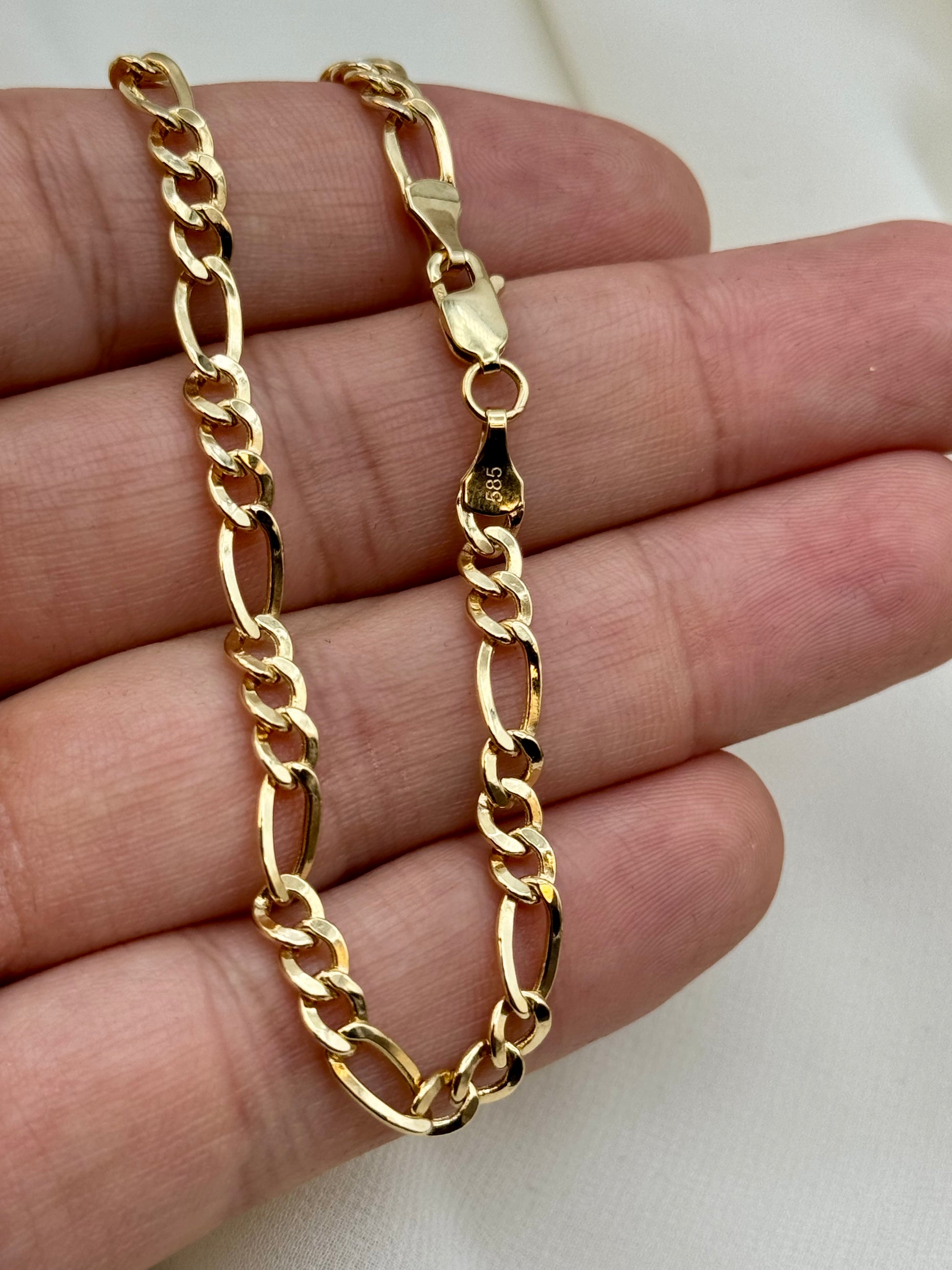 Gold chain necklace held on a hand against a white background
