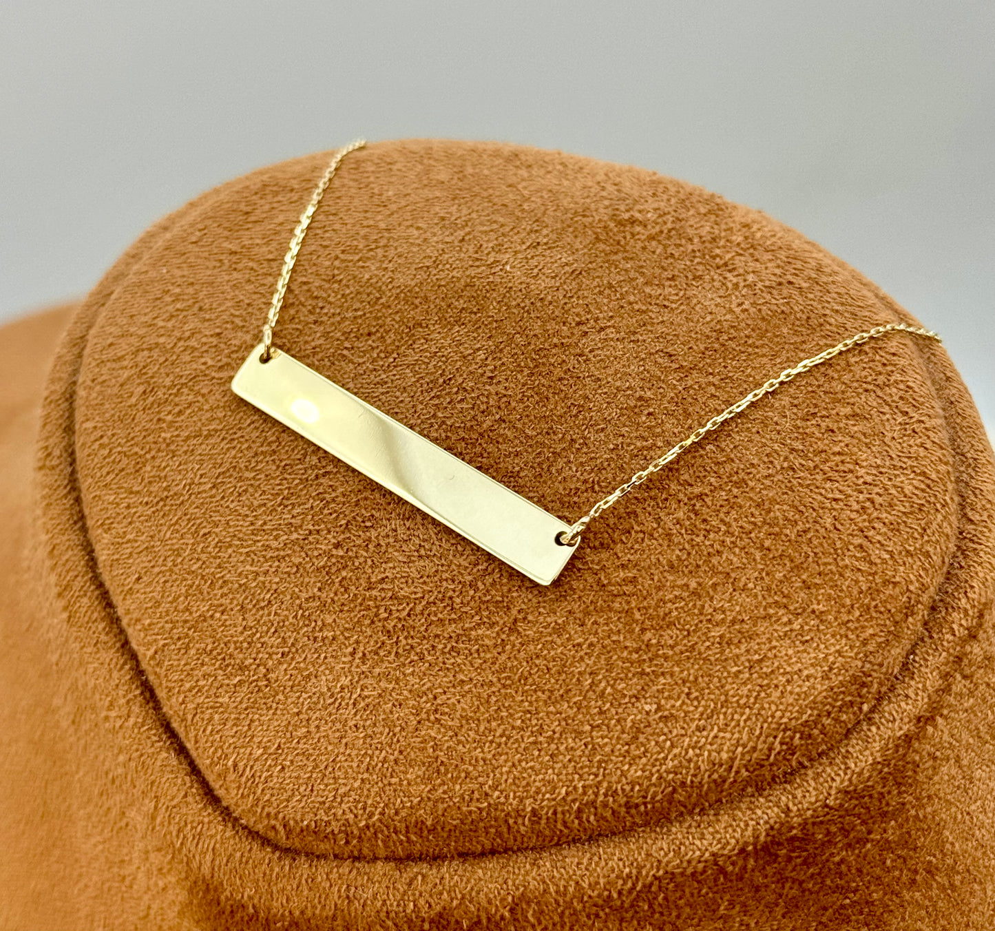 Gold bar necklace on a brown textured surface