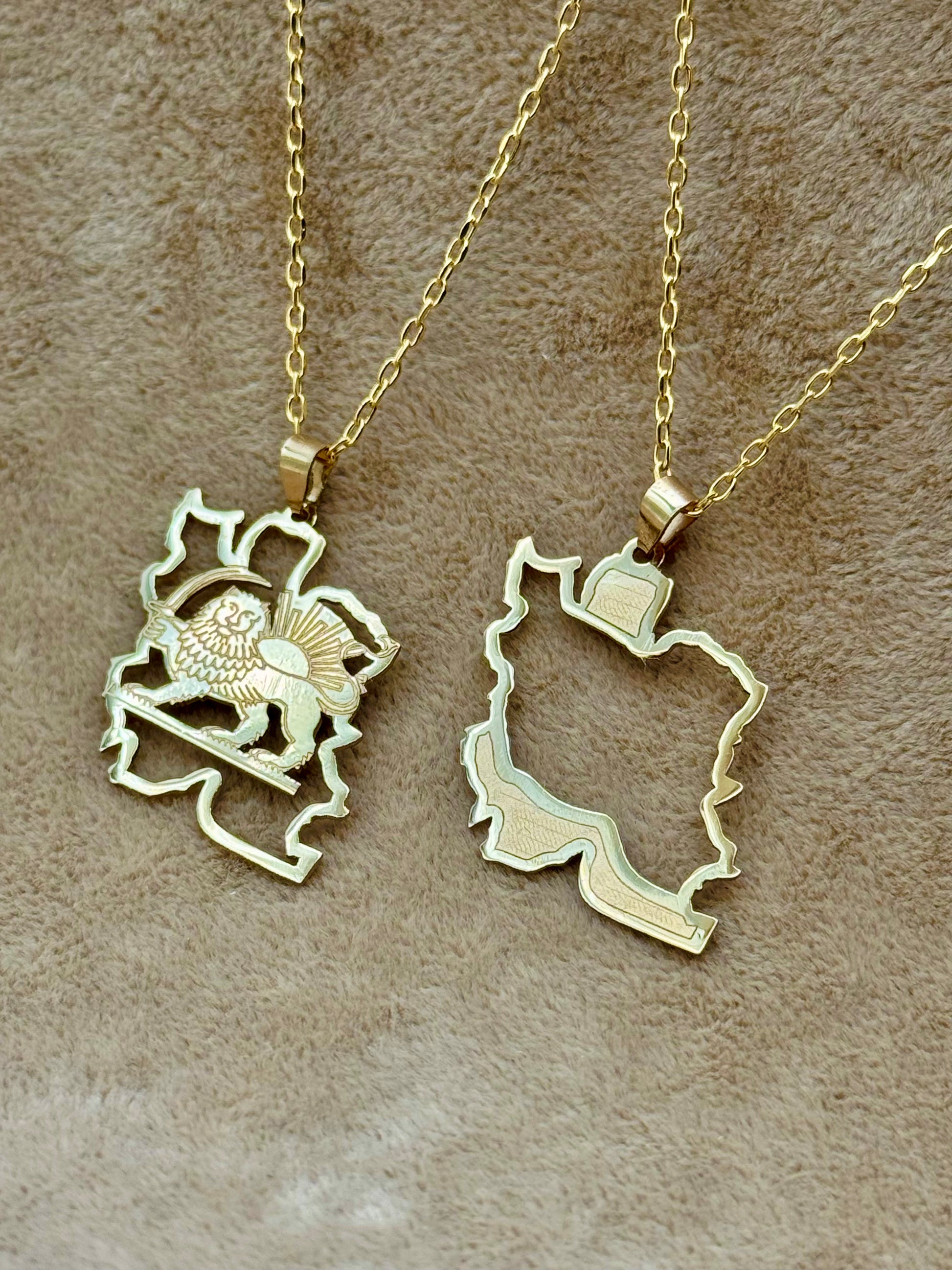 Two gold Persian map necklaces on a brown textured surface
