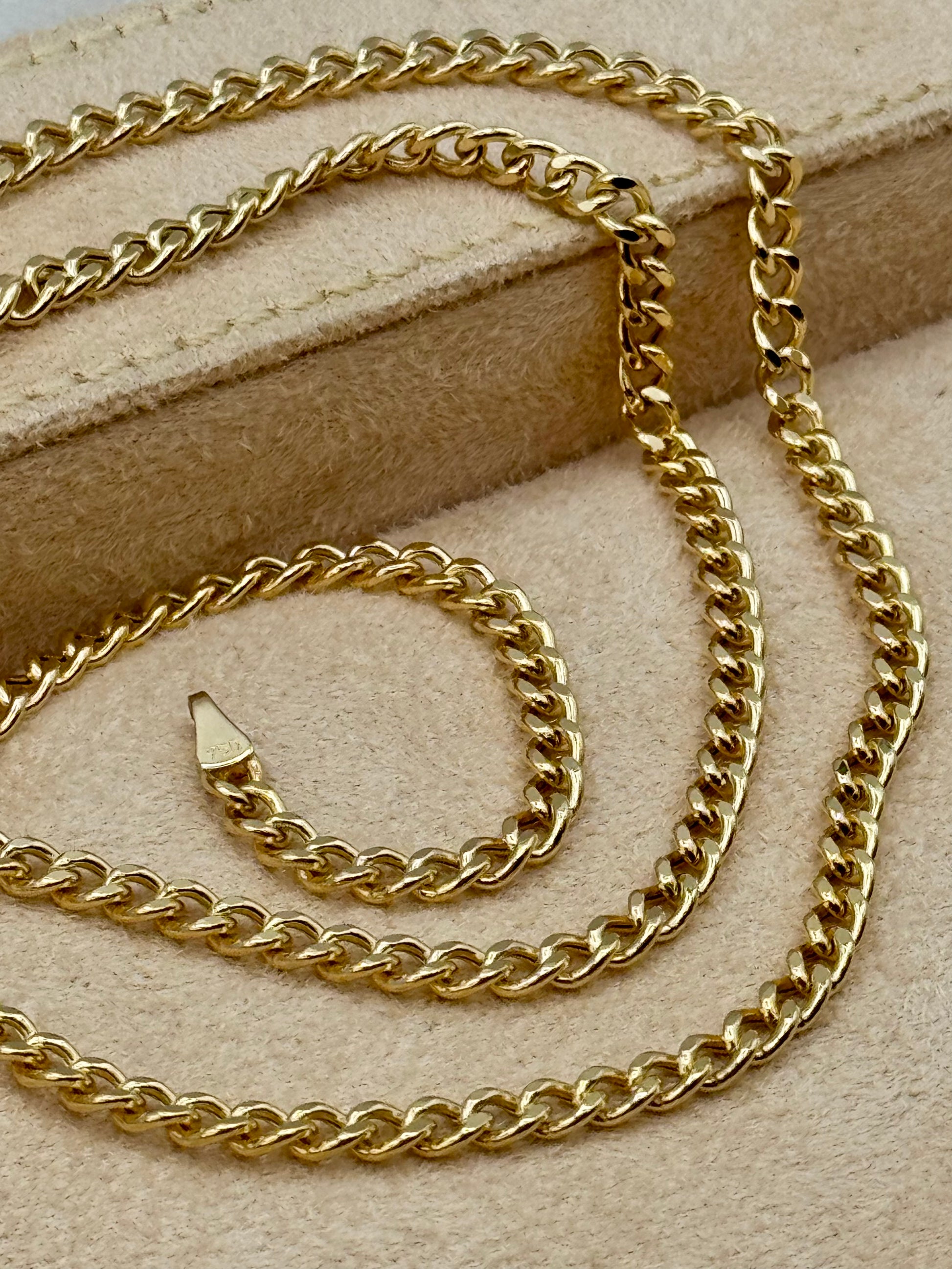 18k Gold curb chain necklace on a beige fabric background