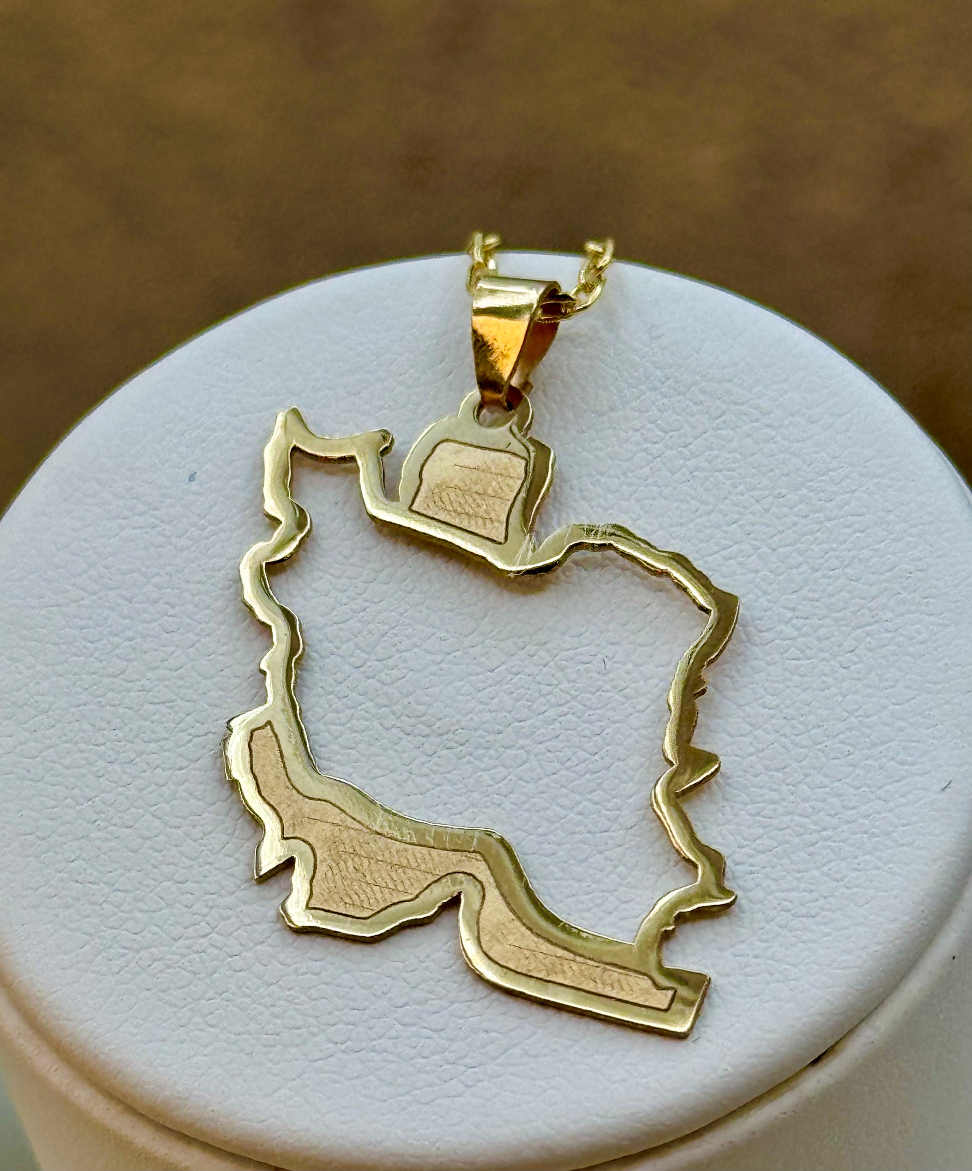 18k Gold pendant shaped like a iran map on a white stand with a brown background