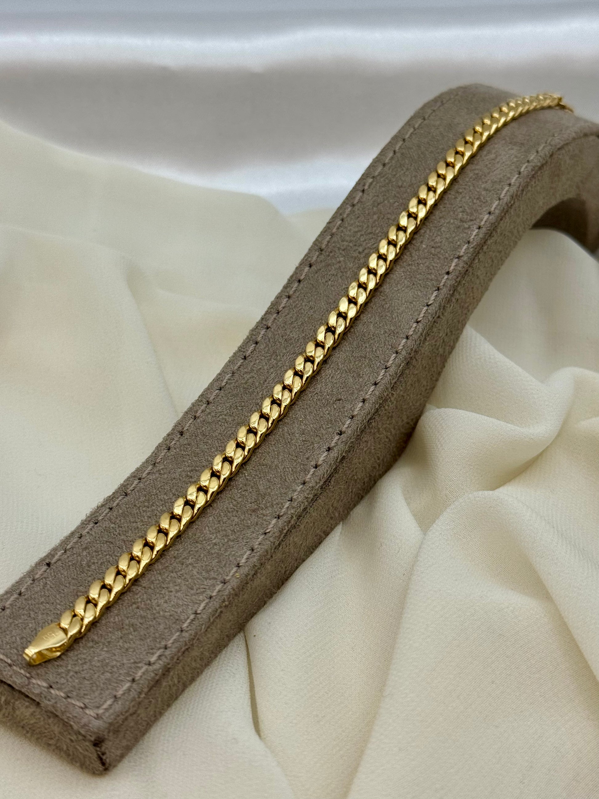 18k Gold curb chain on a brown leather strap against a beige fabric background
