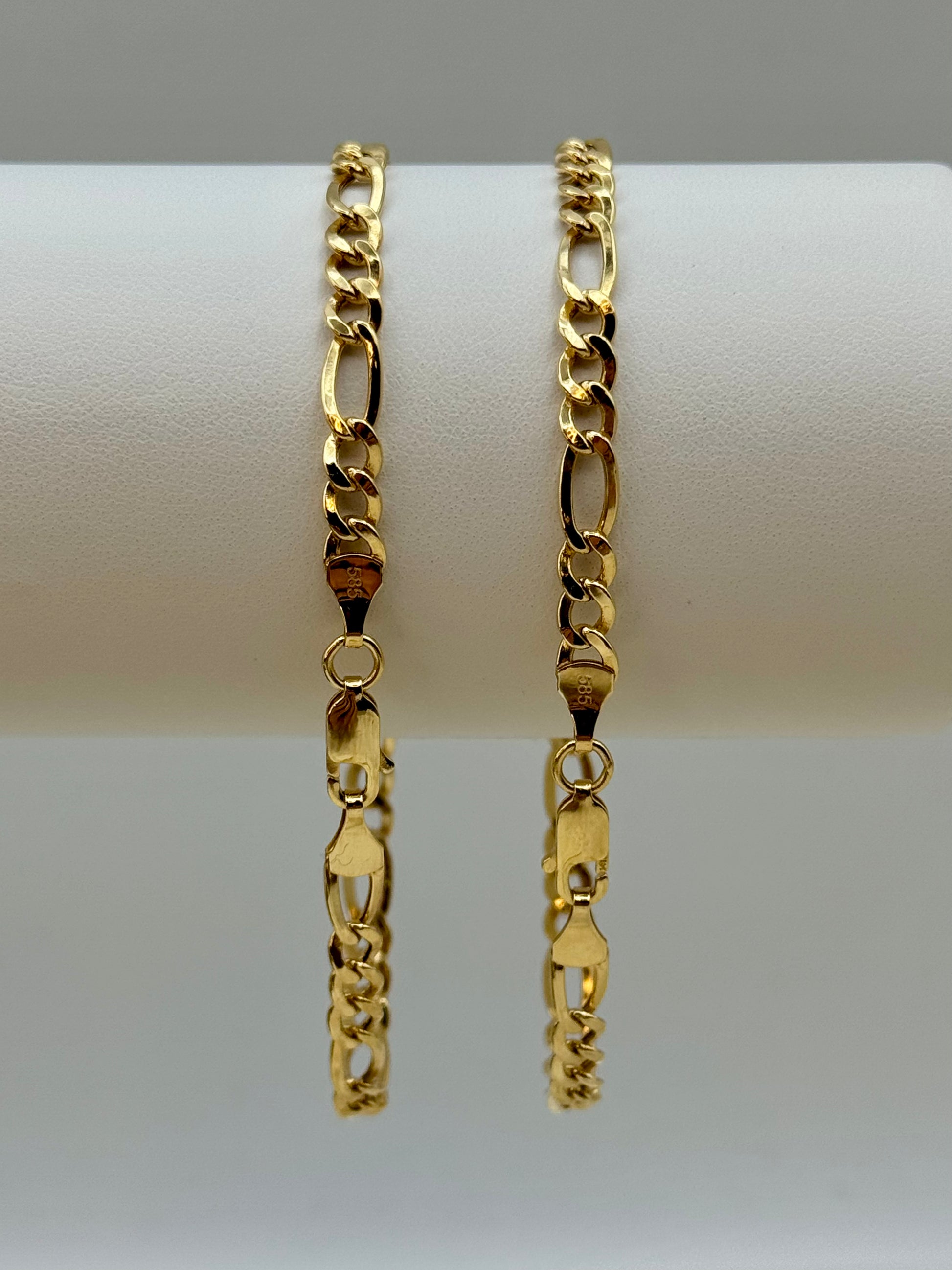 Two gold figaro chain bracelets on a white surface