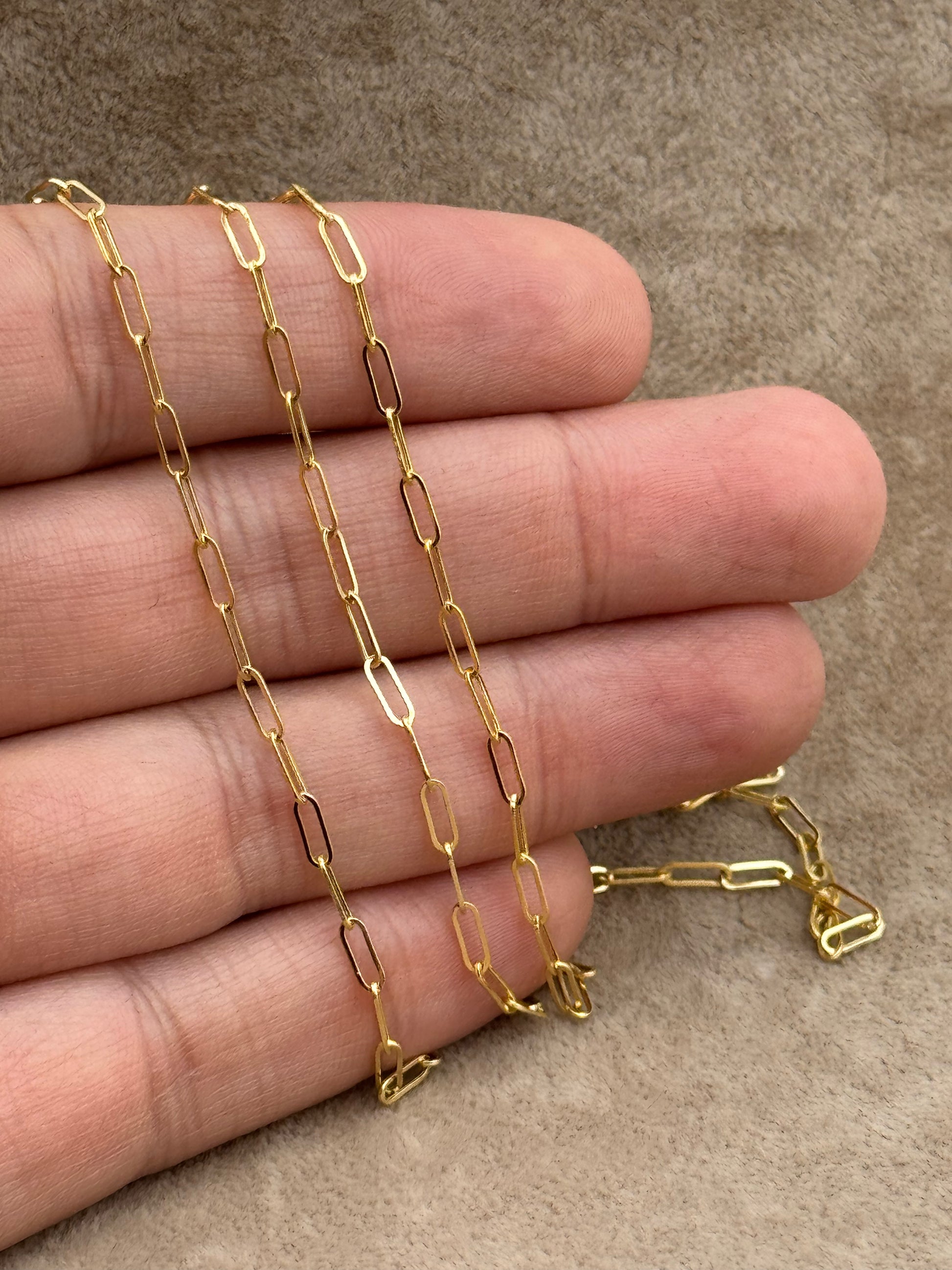 Gold chain held between fingers on a brown background