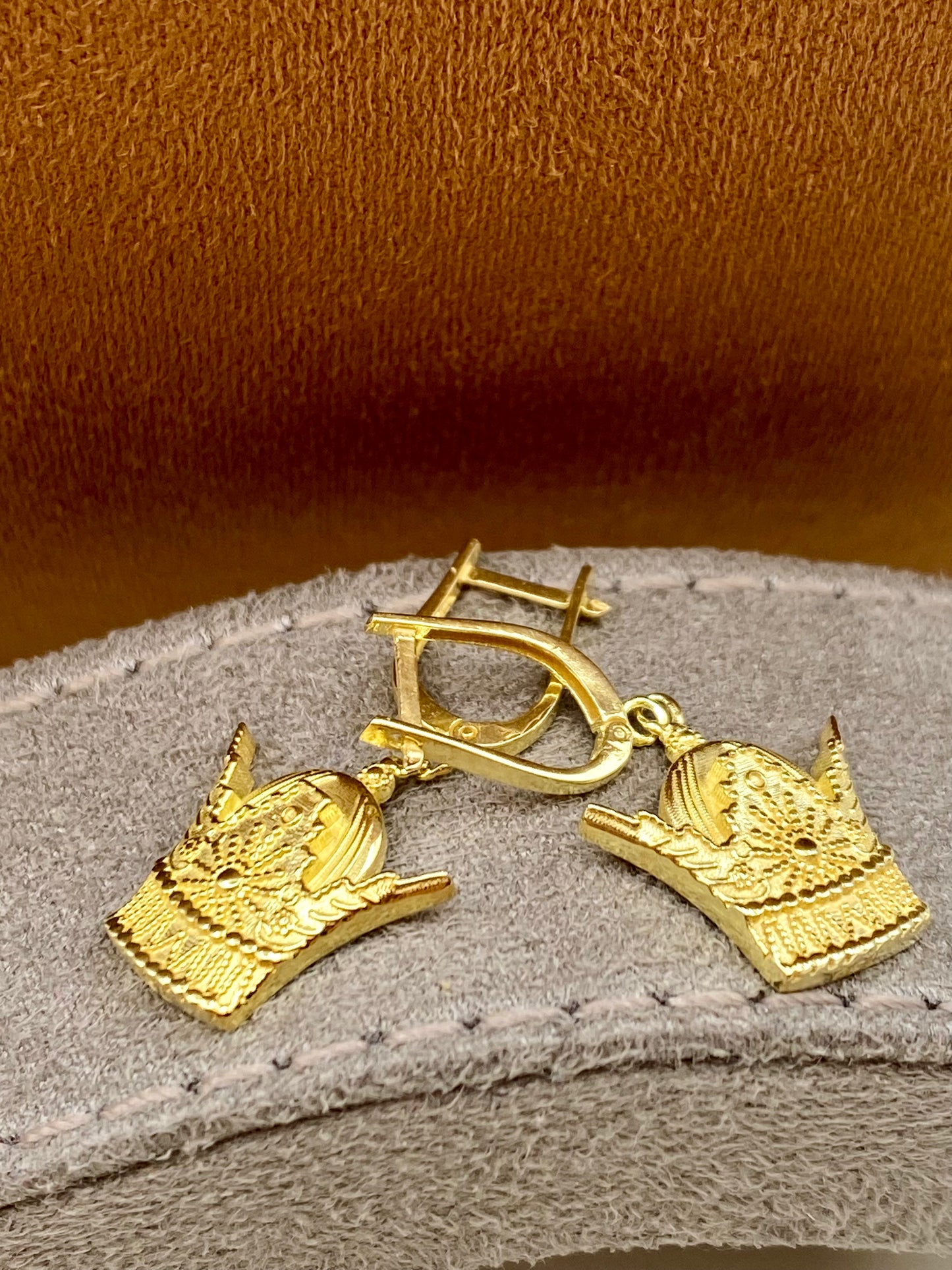 Gold earrings with intricate designs on a textured surface
