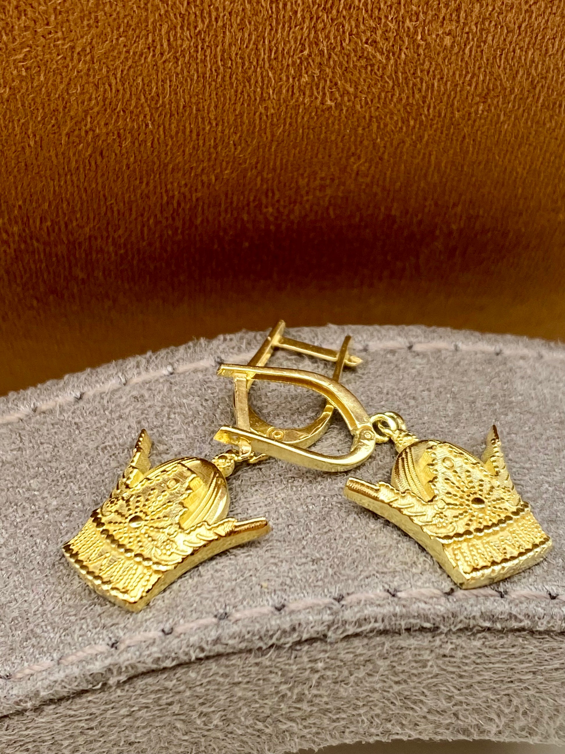 Gold earrings with intricate designs on a textured surface