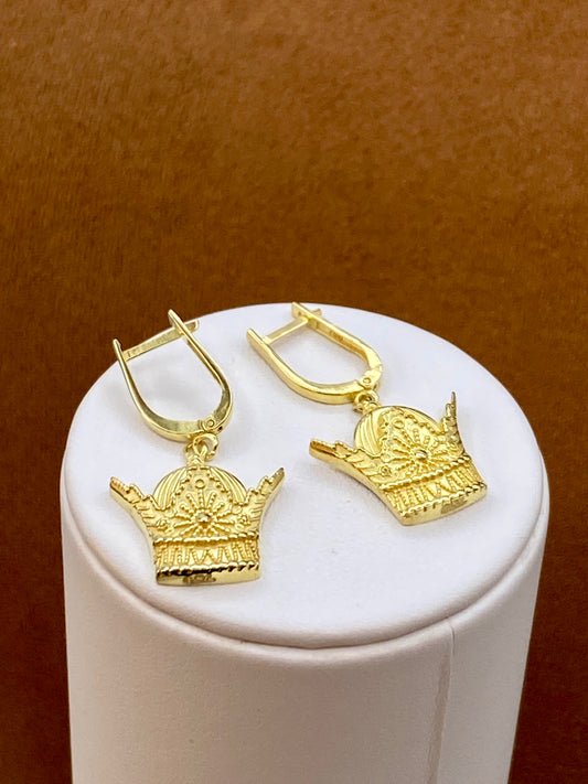 18k Gold crown-shaped earrings on a white cylindrical stand with a brown background