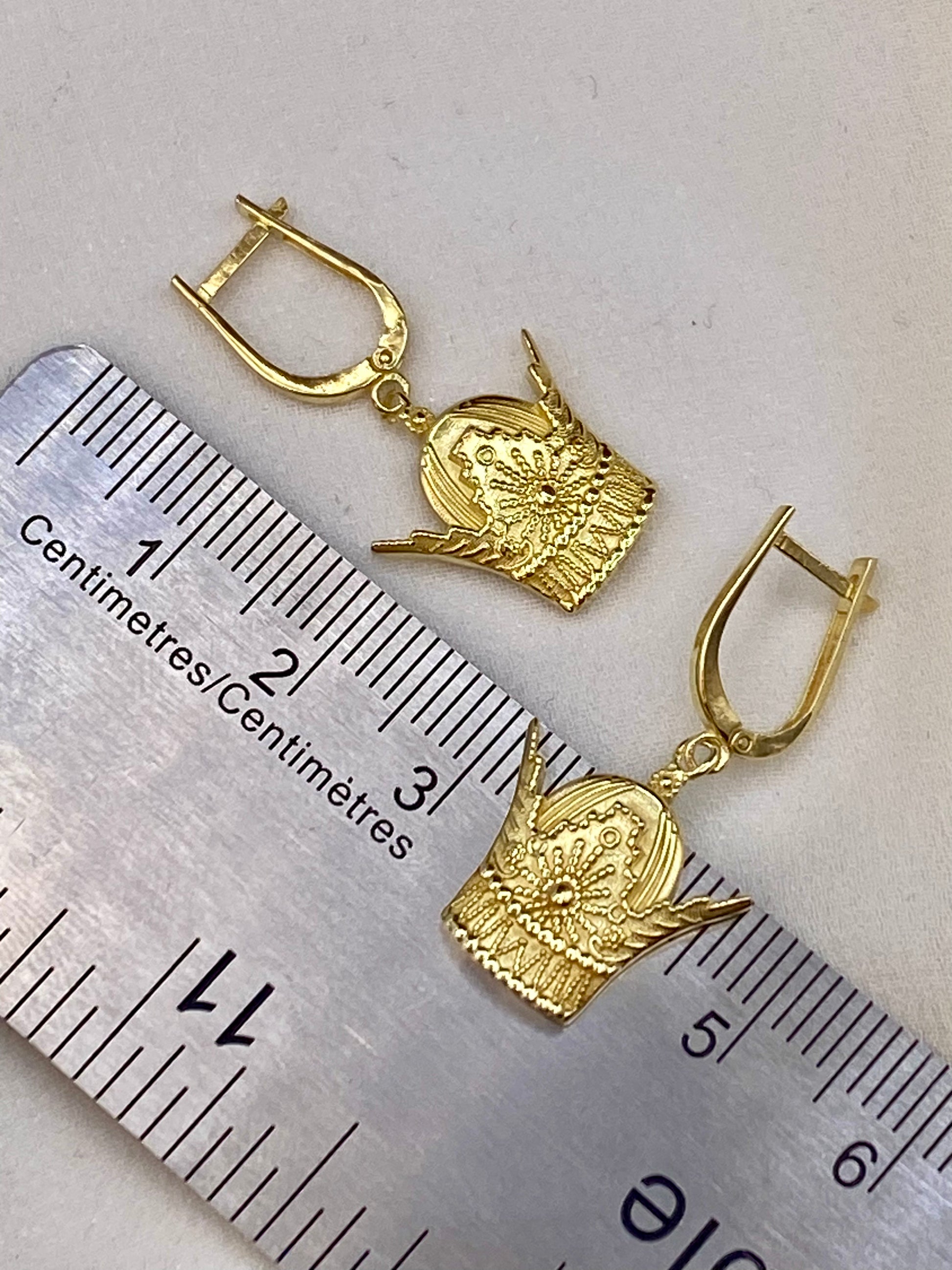 18k Gold earrings with religious design on a ruler for scale