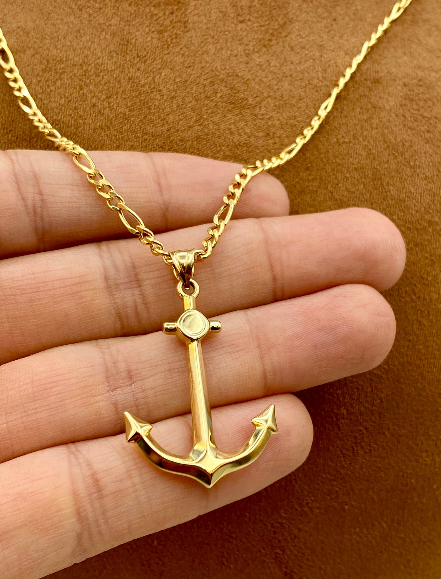 Gold anchor necklace on a hand against a brown background