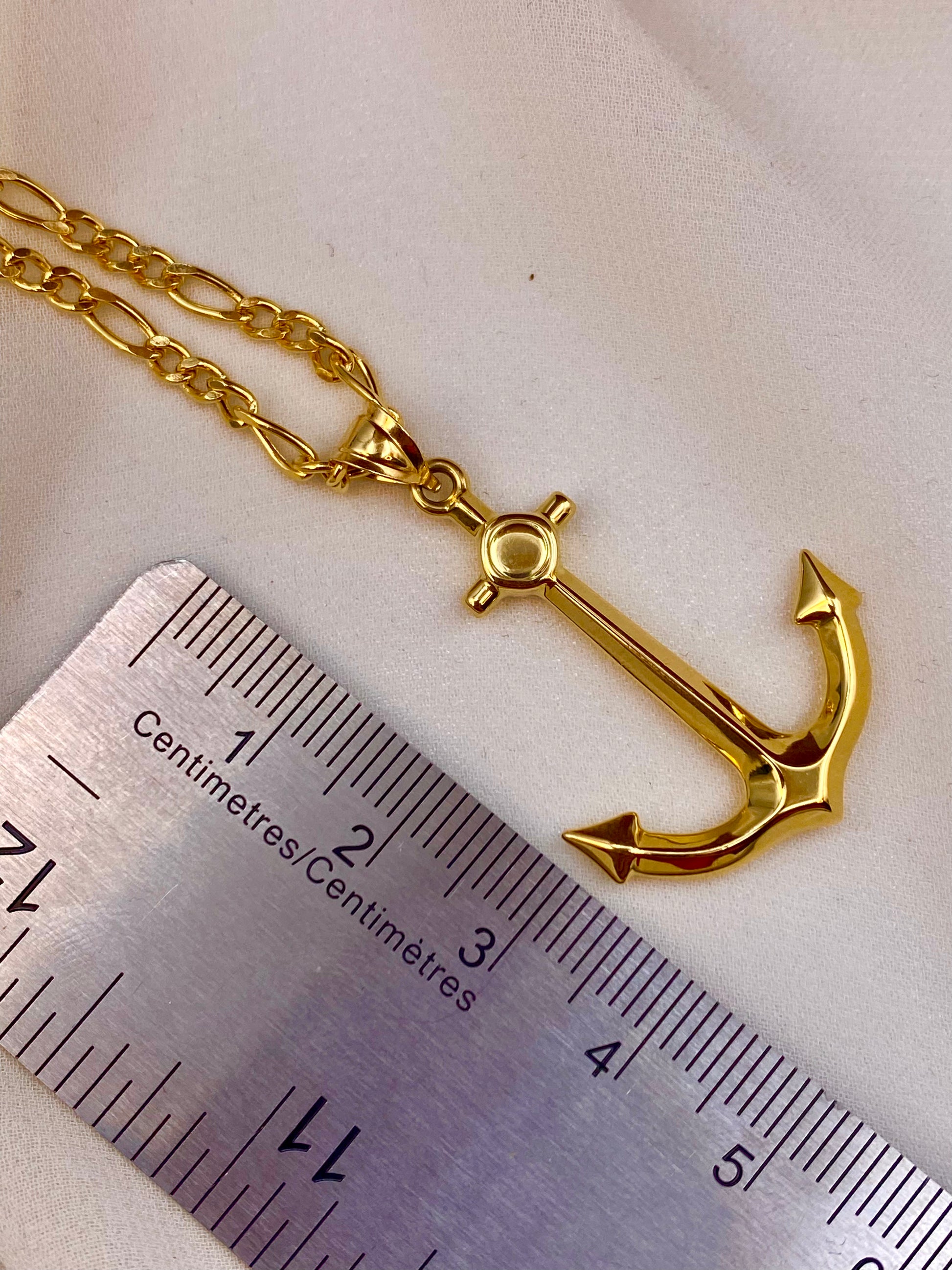 Gold anchor necklace next to a ruler on a light background