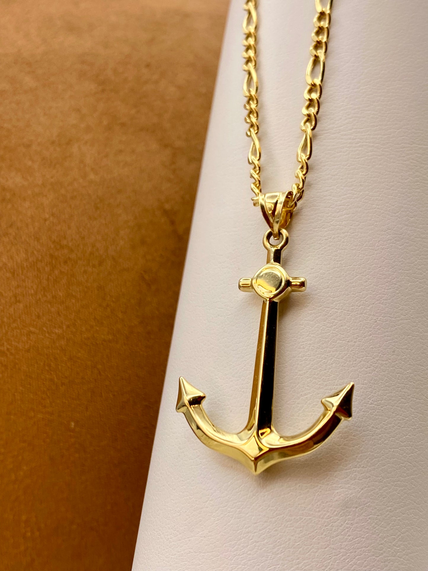 Gold anchor necklace on a light pink surface with a brown background