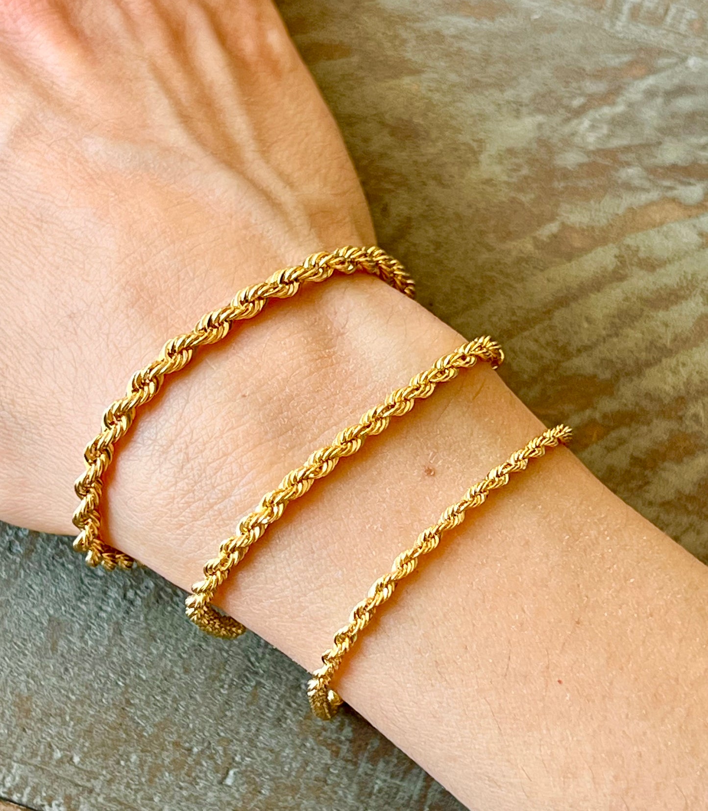 Gold bracelets on a wrist against a neutral background
