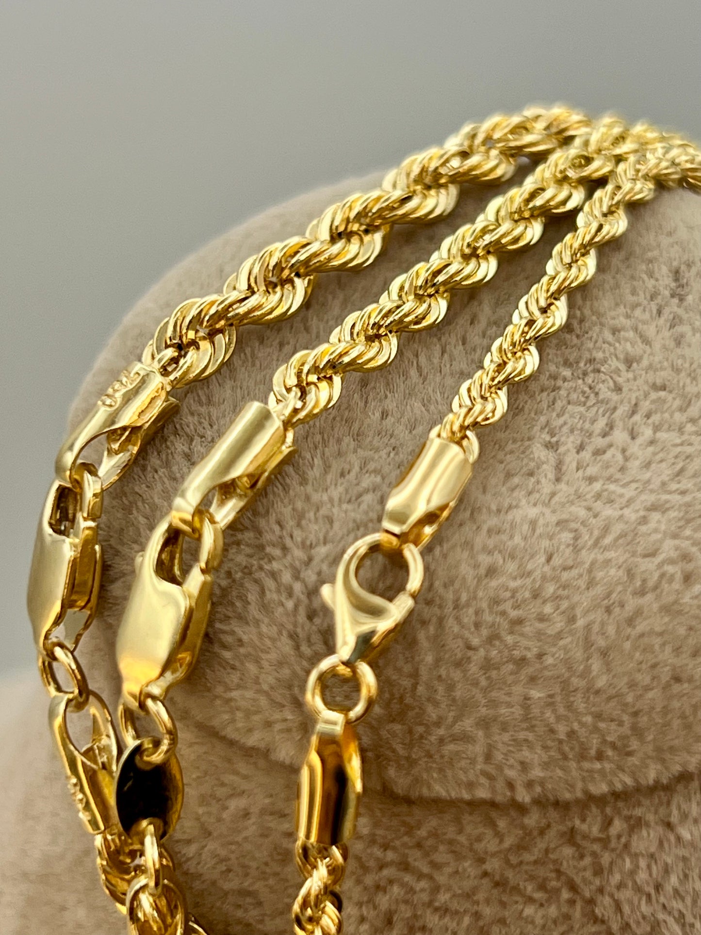 Two gold chains on a textured beige surface