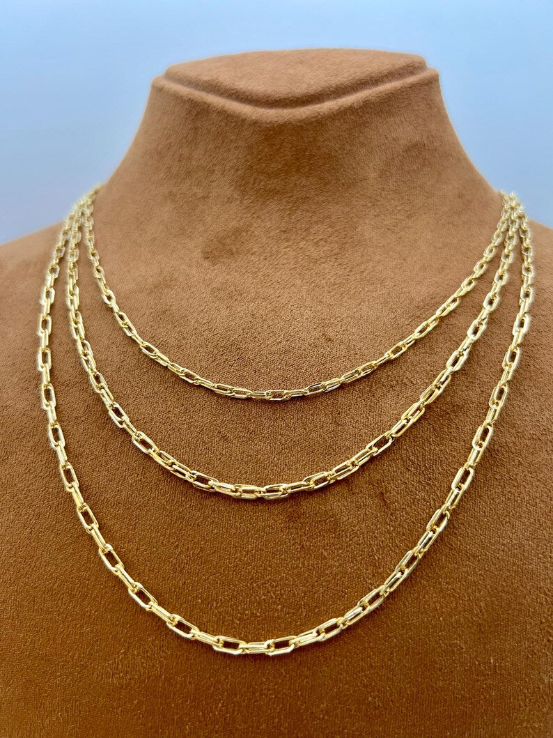 A gold-toned multi-strand chain necklace displayed on a brown velvet jewelry bust against a light blue background.