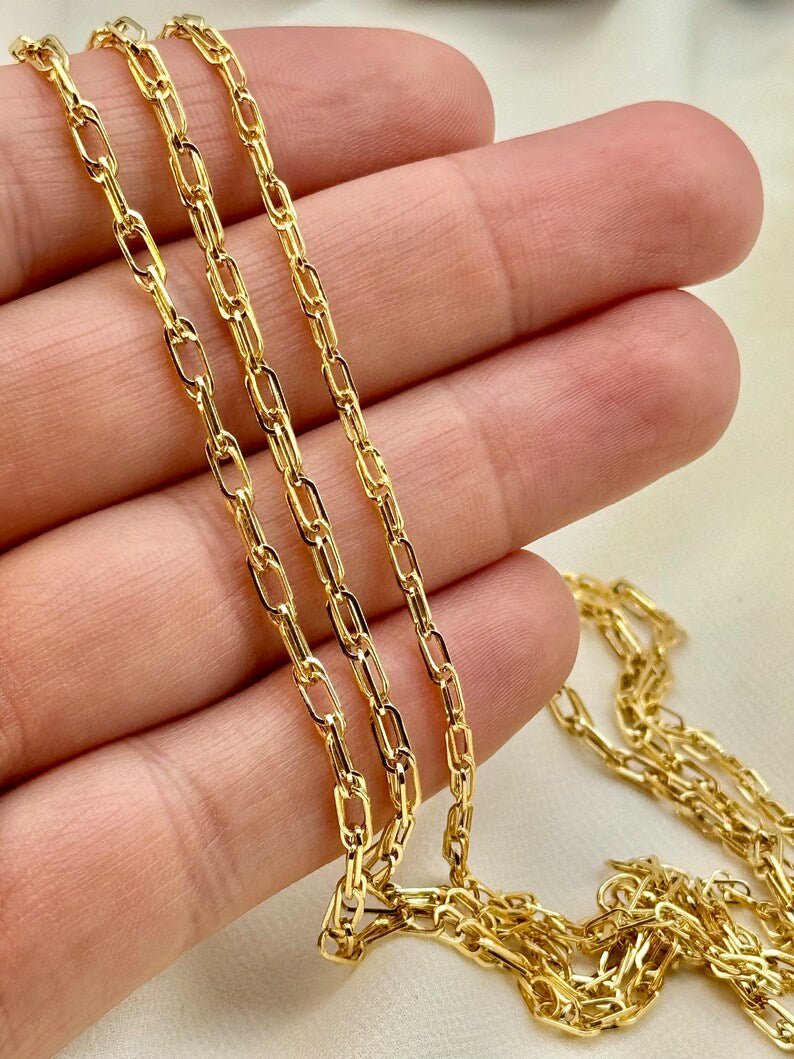 A close-up of a gold chain necklace draped over a person's hand, showing the chain's link pattern and texture against a light neutral background.