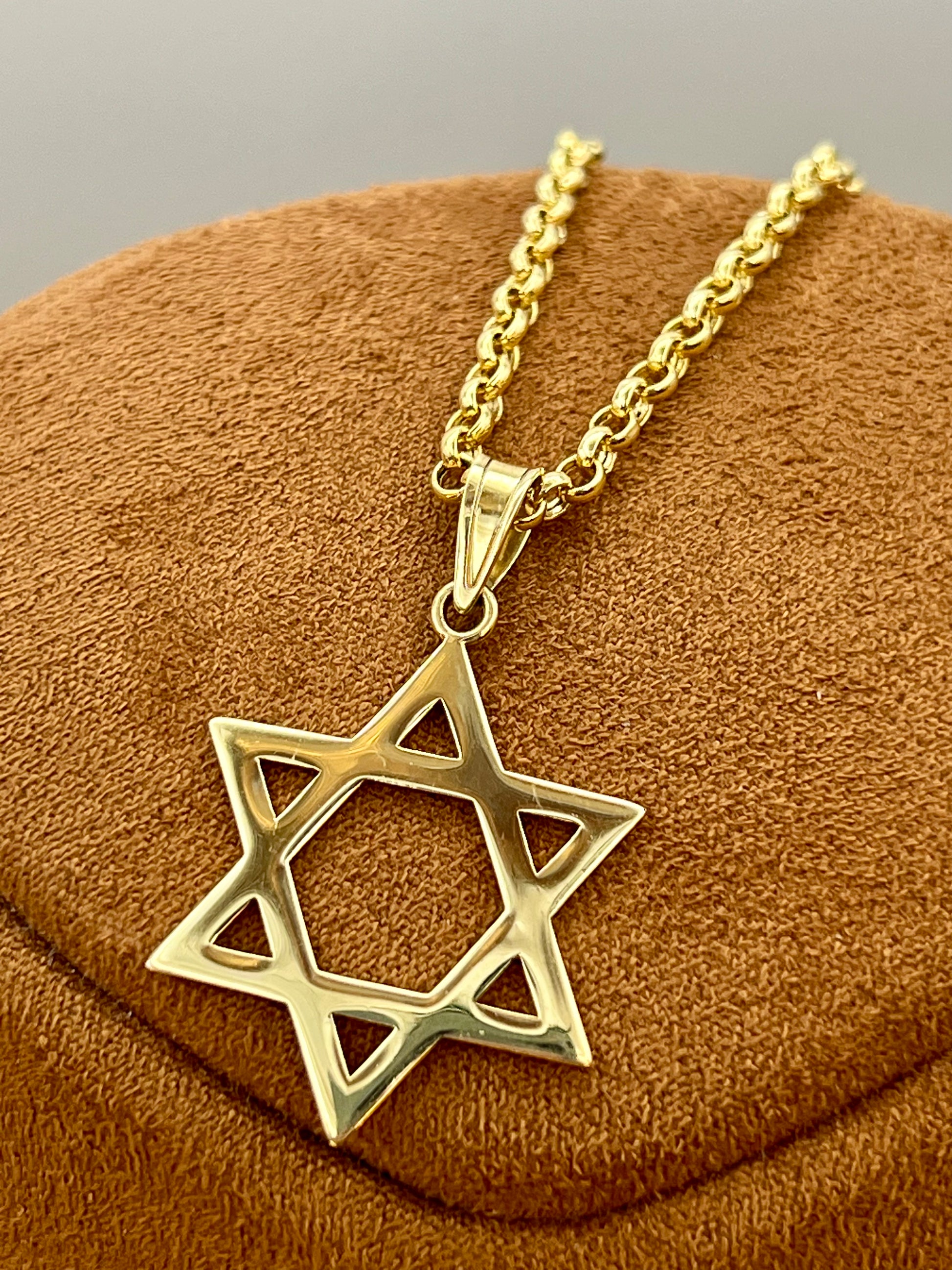 A gold Star of David pendant necklace on a matching gold chain, displayed on a brown textured velvet jewelry stand.