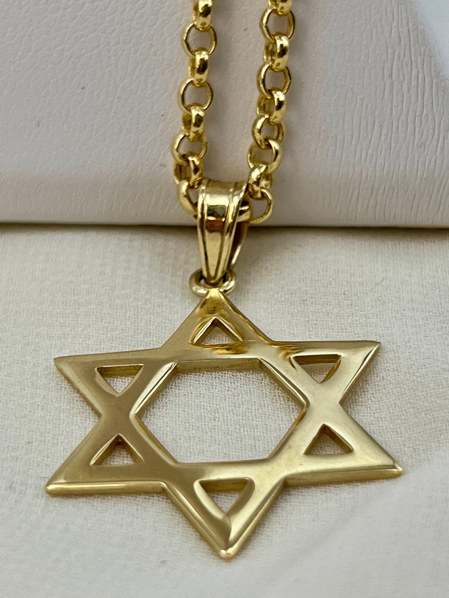 A gold Star of David pendant necklace on a matching gold chain, displayed on a textured off-white surface.