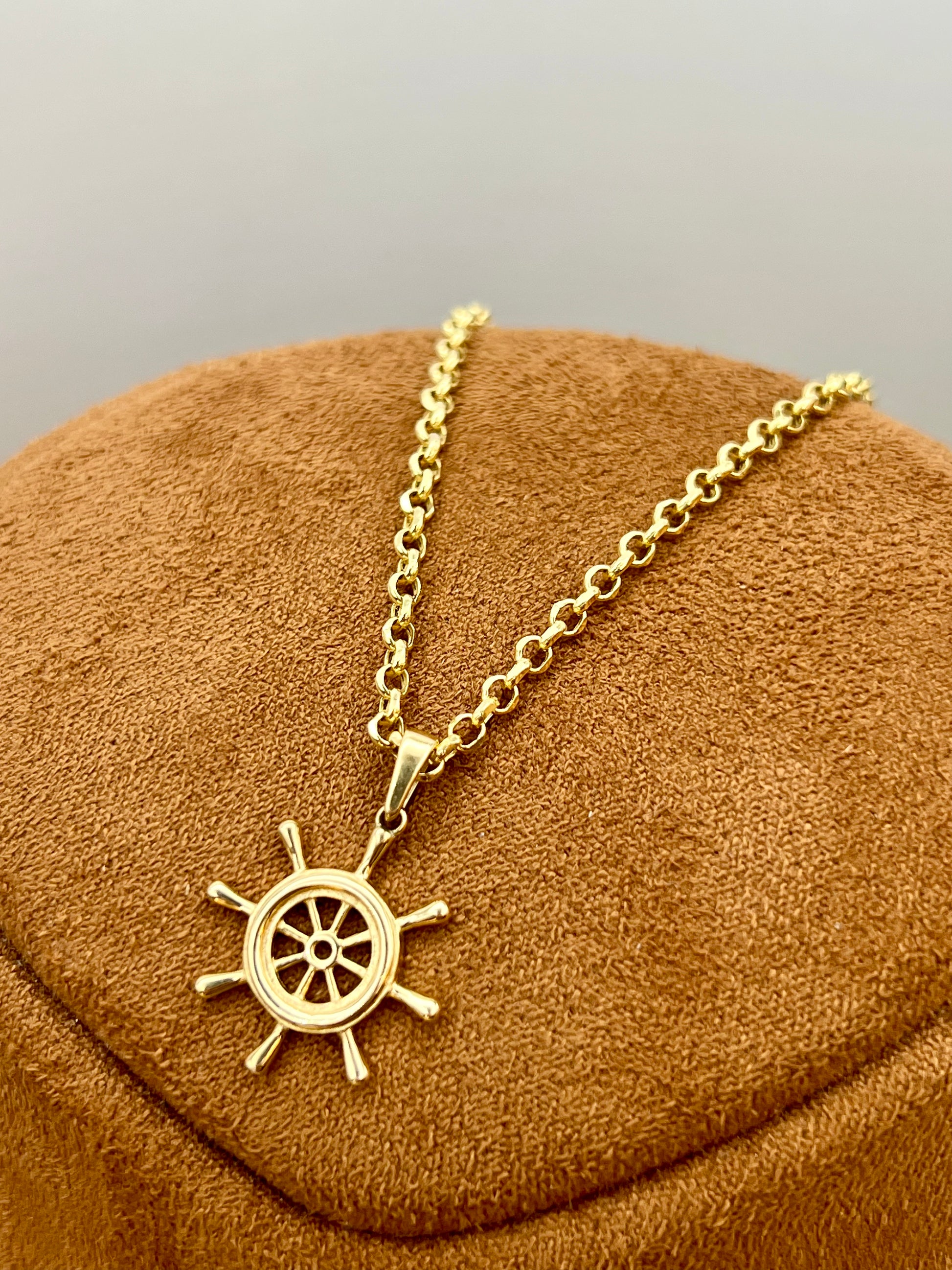 A gold ship's wheel pendant necklace displayed on a brown velvet jewelry bust against a neutral gray background.
