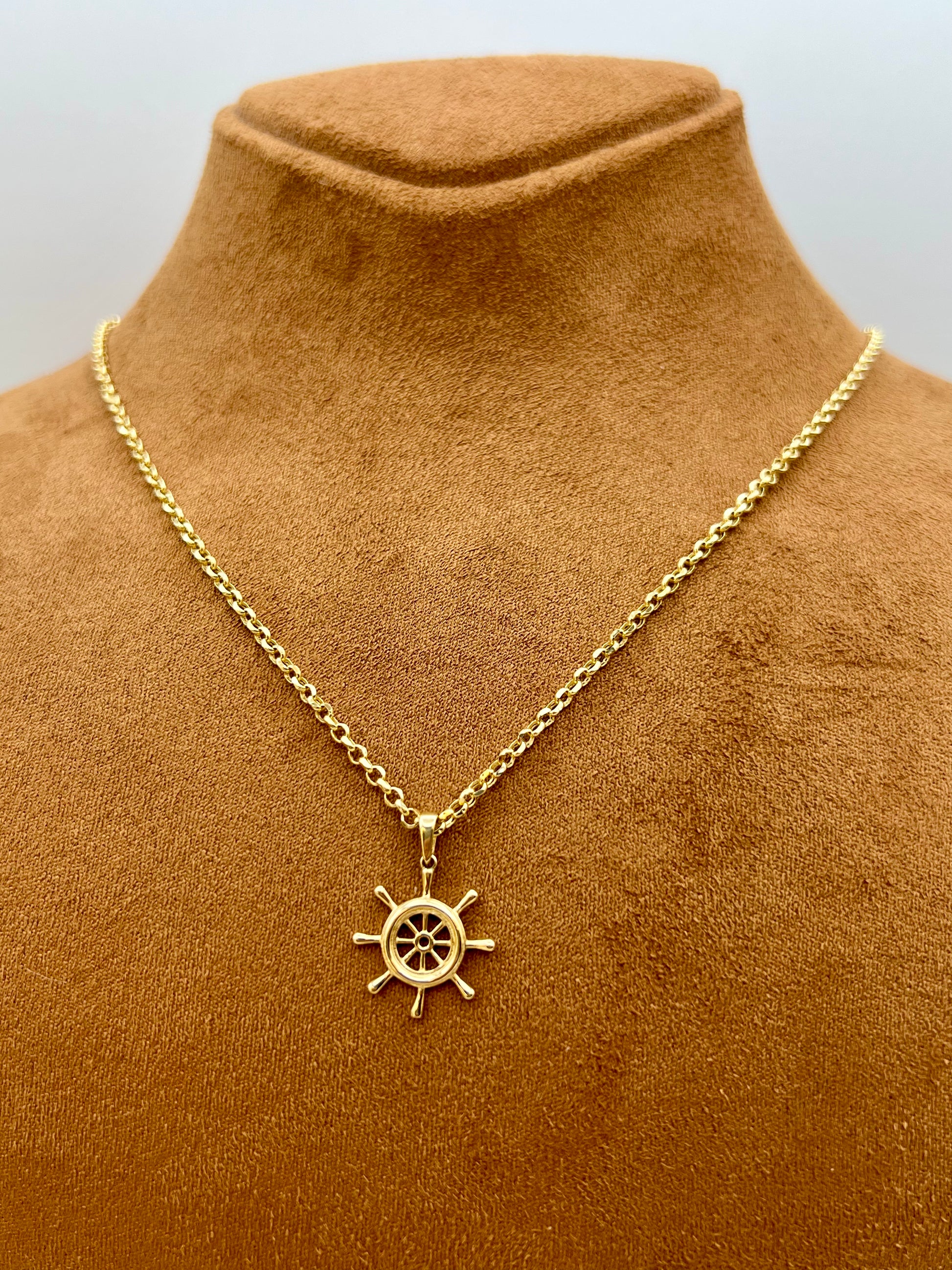 A gold chain necklace with a ship's wheel pendant, displayed on a brown velvet jewelry bust against a light gray background.